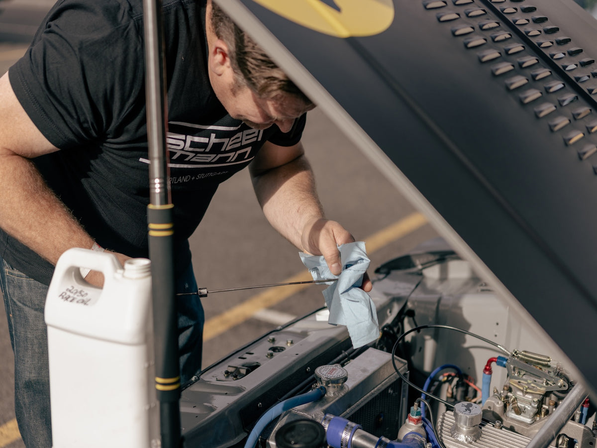 Black scheel-mann stacked logo tee, checking engine oil on Ford Cortina vintage race car
