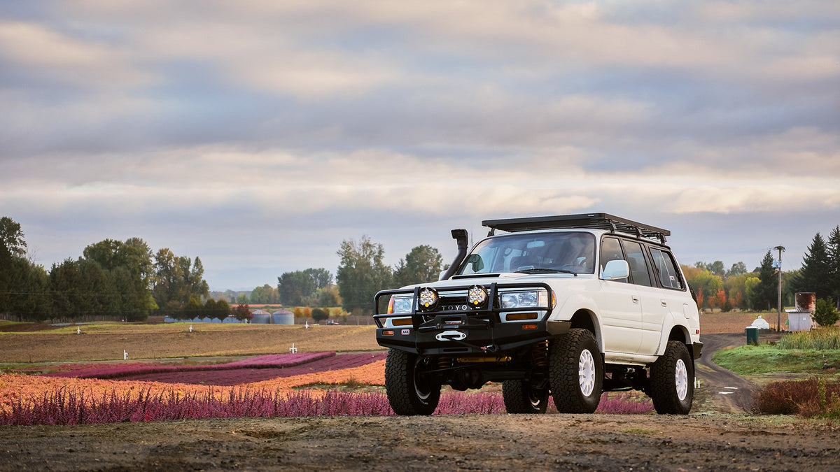 White lifted Toyota 80 Series Land Cruiser in farm field of flowers and partially cloudy sky