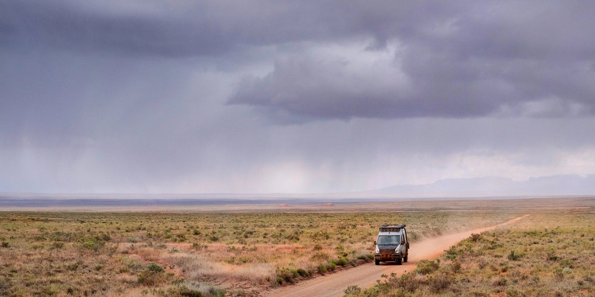 Mercedes Sprinter Van traveling along a dirt road in the desert with a stormy sky and rain in the background