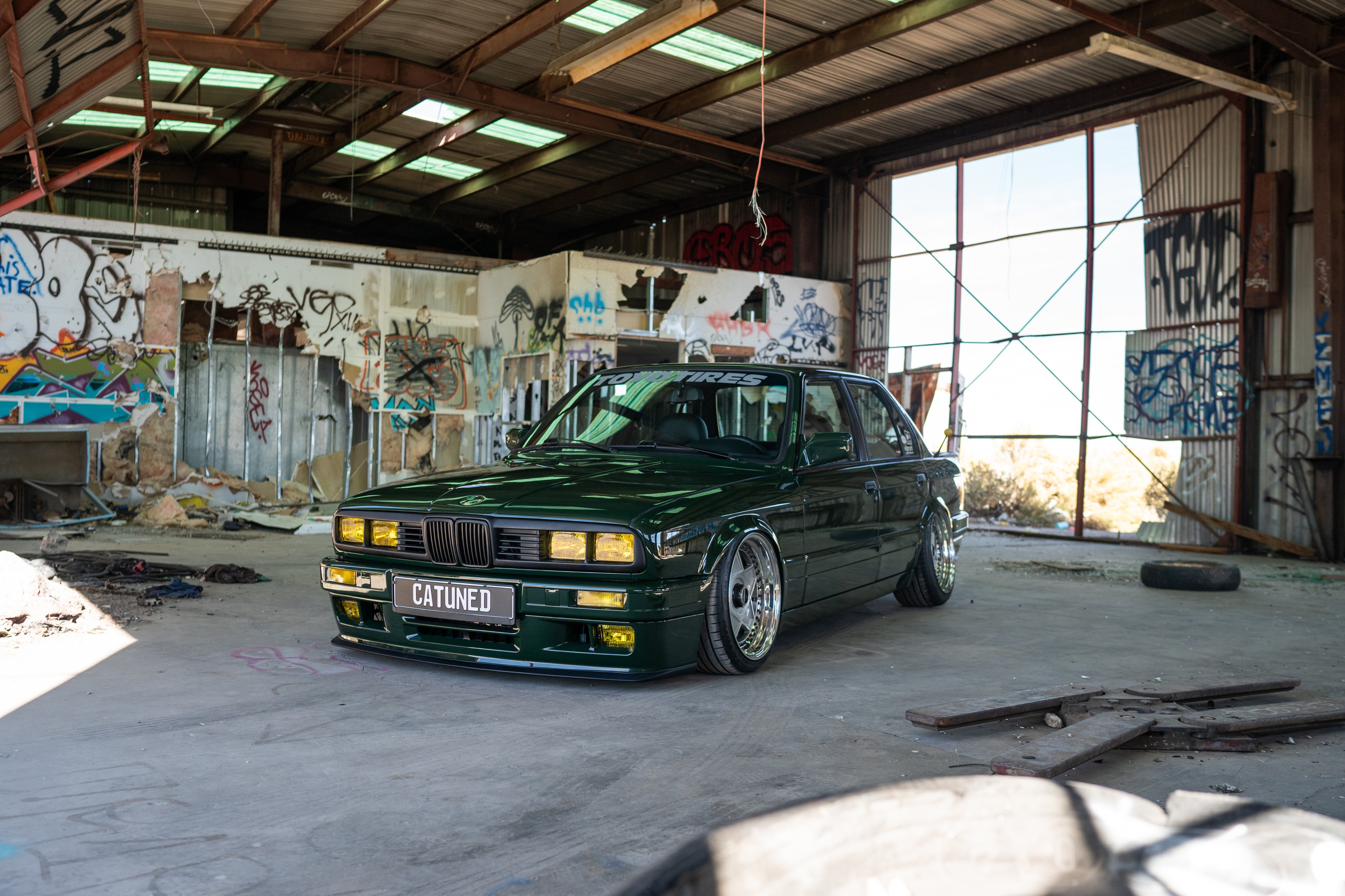 Green BMW E30 front hero shot of entire car in an abandoned workshop in the desert.