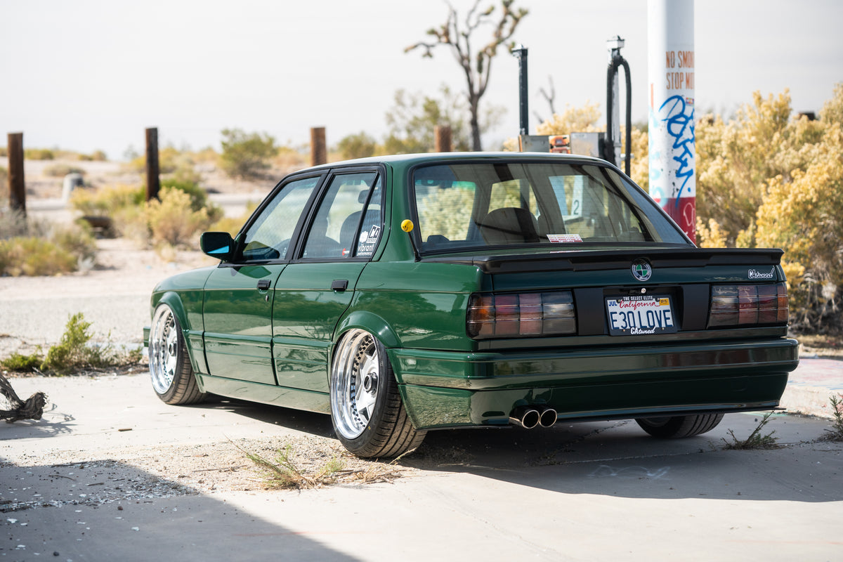 Green BMW E30 rear hero parked outside of an old abandoned gas station in the desert